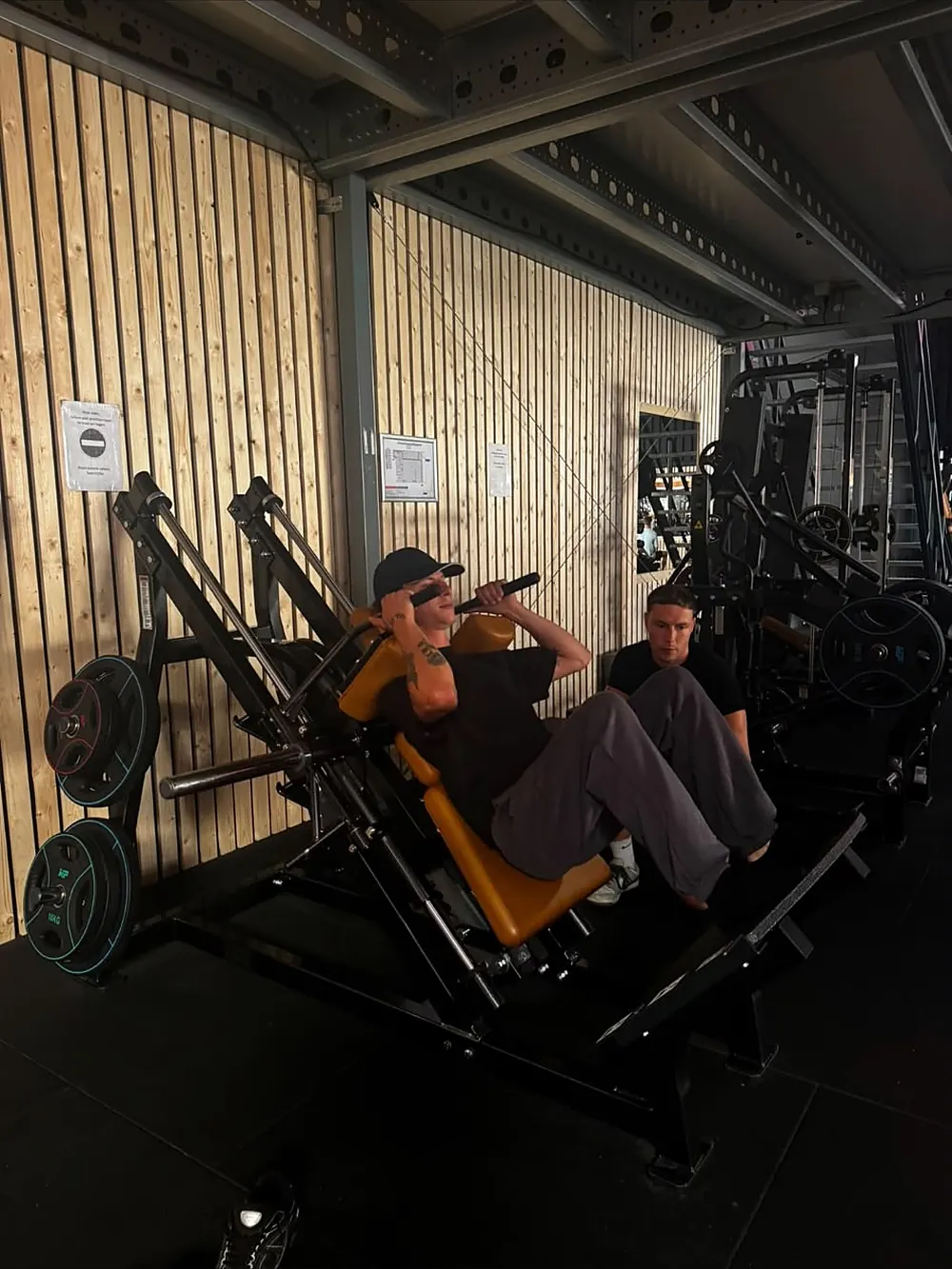Dion kijkt mee bij de leg press terwijl een cliënt de set doet